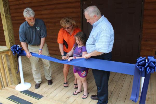 (From left) Owen Wright, Pat Griffith, and Guy Adams assist second-year camper Natalee with cutting the ribbon at the dedication of Bradford Hall, the new girls’ dormitory at Camp Shawnee.